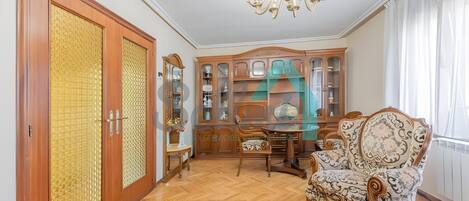 A room with a wooden floor, a large armoire, a dining table with chairs, and a patterned armchair.