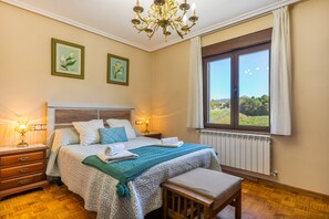 Ein Schlafzimmer mit einem großen Bett, Nachttischlampen, einer hölzernen Bank, einem Heizkörper und zwei gerahmten Blumenbildern an der Wand.
