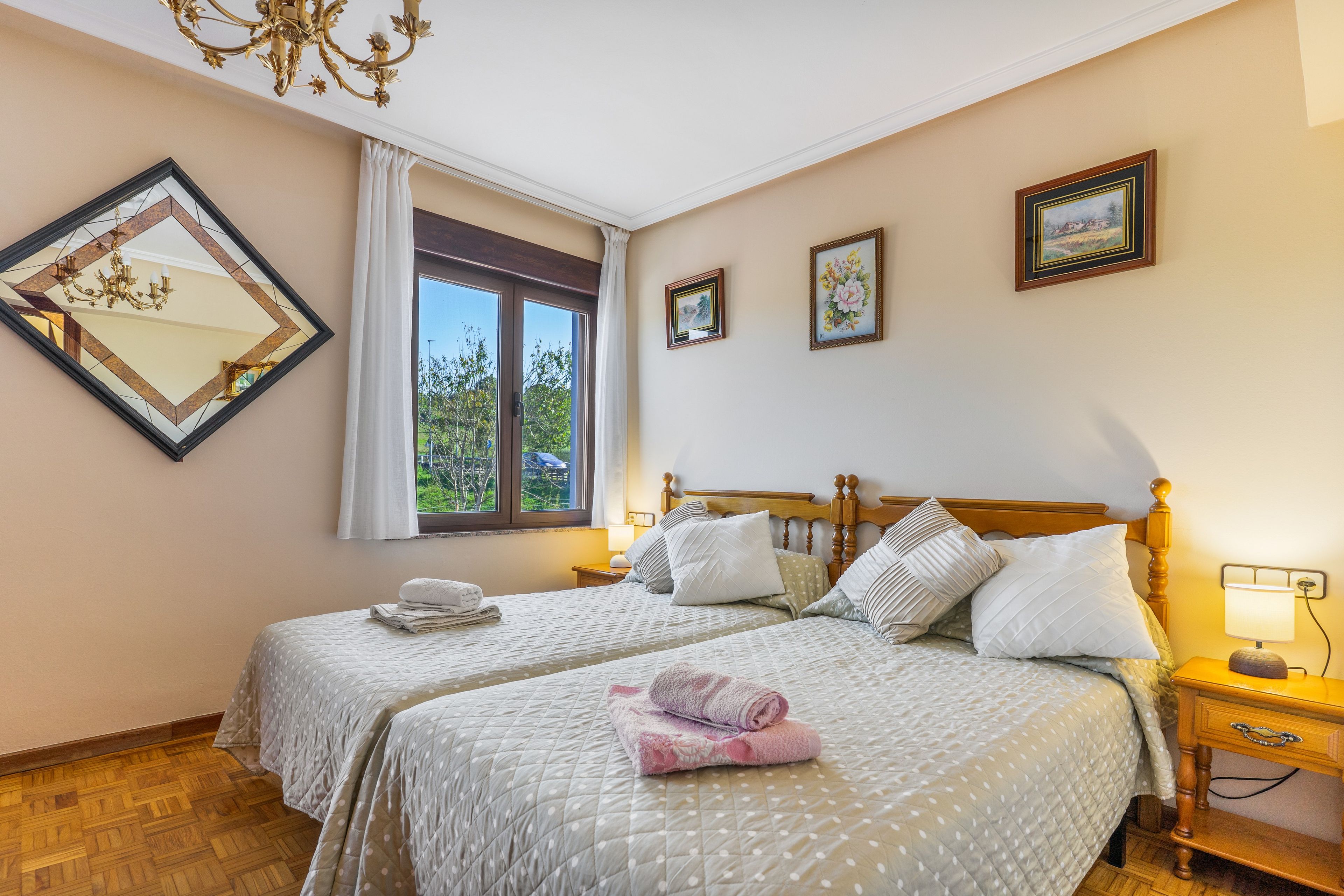 Een hotelkamer met twee bedden, een grote spiegel, een kroonluchter en een raam met uitzicht op groen.