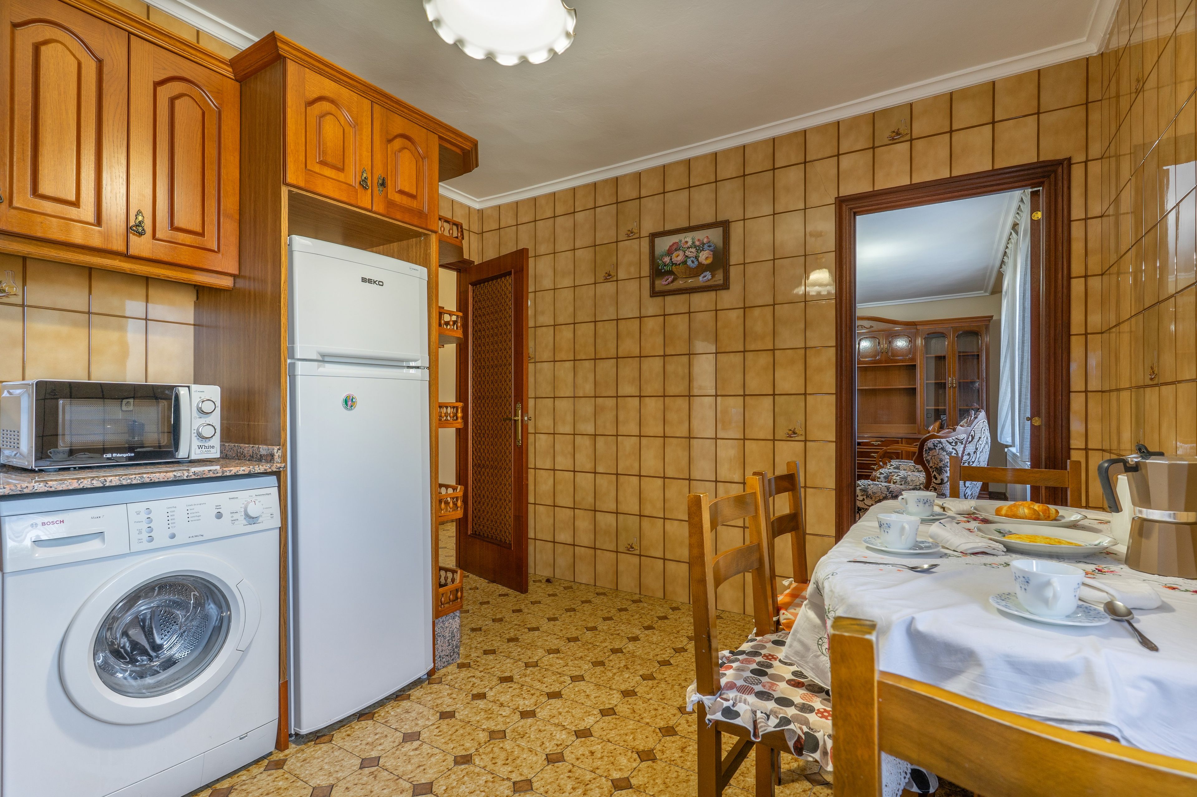 Una cocina con armarios de madera, un refrigerador blanco, un microondas y una lavadora.