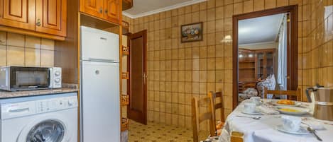 Una cocina con armarios de madera, un refrigerador blanco, un microondas y una lavadora.
