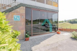 A modern building with a large glass entrance, a sign with letters 'VV', and a view of a green slide and vehicles outside.