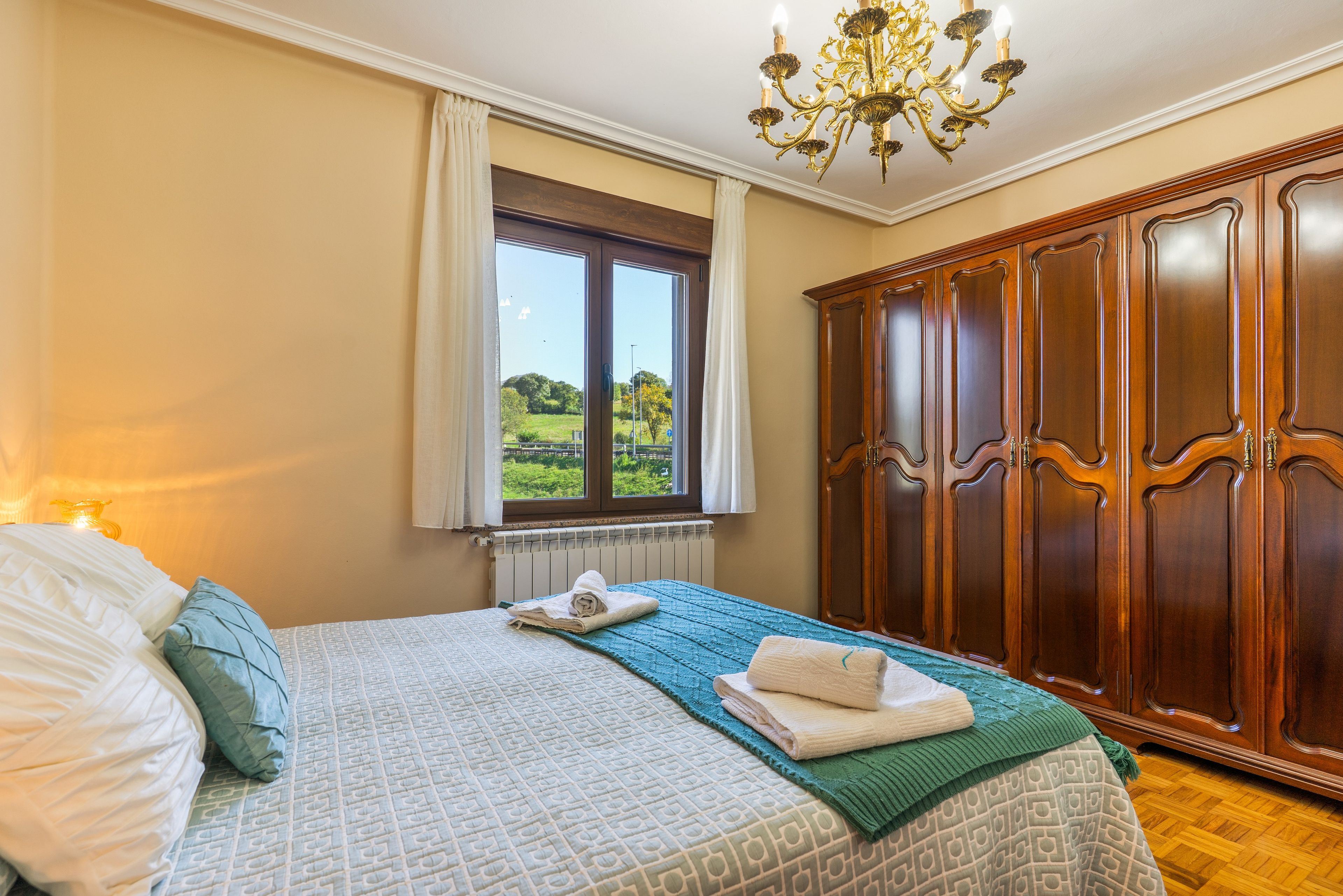 Un dormitorio con una cama grande, un armario, una ventana con vistas y una araña.