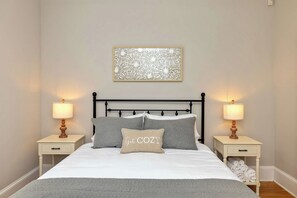 A neatly made bed with a grey blanket, two bedside lamps, a decorative wall piece, and a bedside table with a rolled towel. - Historic Dilworth Home - Short Walk to South End (Charlotte)