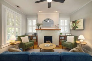 A living room with a fireplace, two green armchairs, a blue sofa, and a round coffee table. - Historic Dilworth Home - Short Walk to South End (Charlotte)