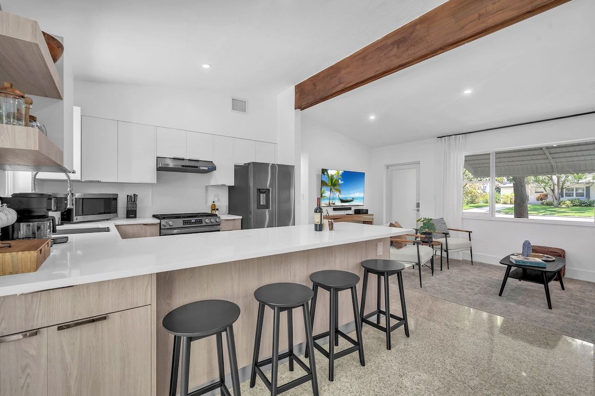 A modern kitchen with a central island, bar stools, and a dining area with a view.