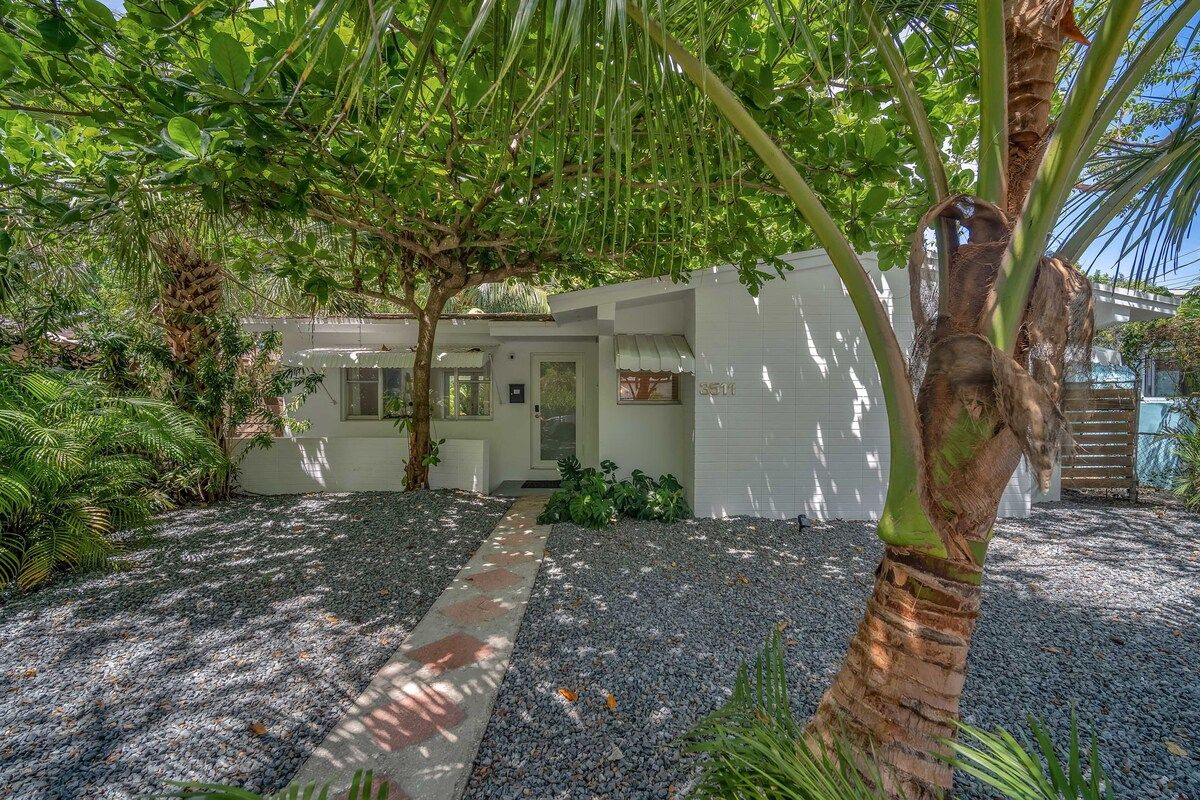 Ein Haus mit Kiesweg, umgeben von üppigem Grün und einer Palme.