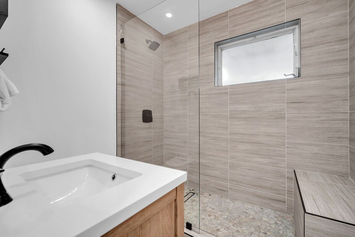 Ein modernes Badezimmer mit einem weißen Waschbecken, einer Duschkabine und einem kleinen Fenster.