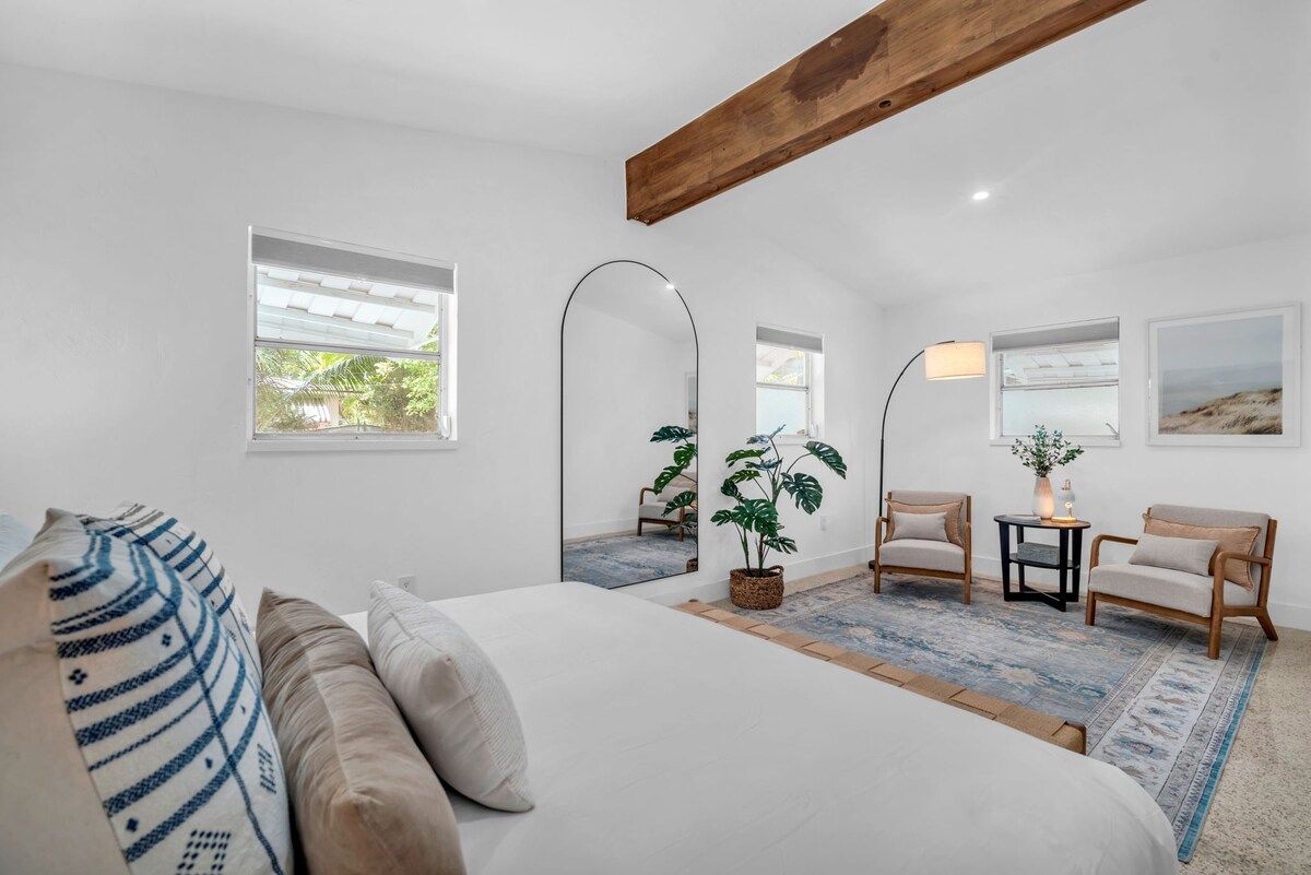 A modern bedroom with a bed, two chairs, a small table, and a mirror.