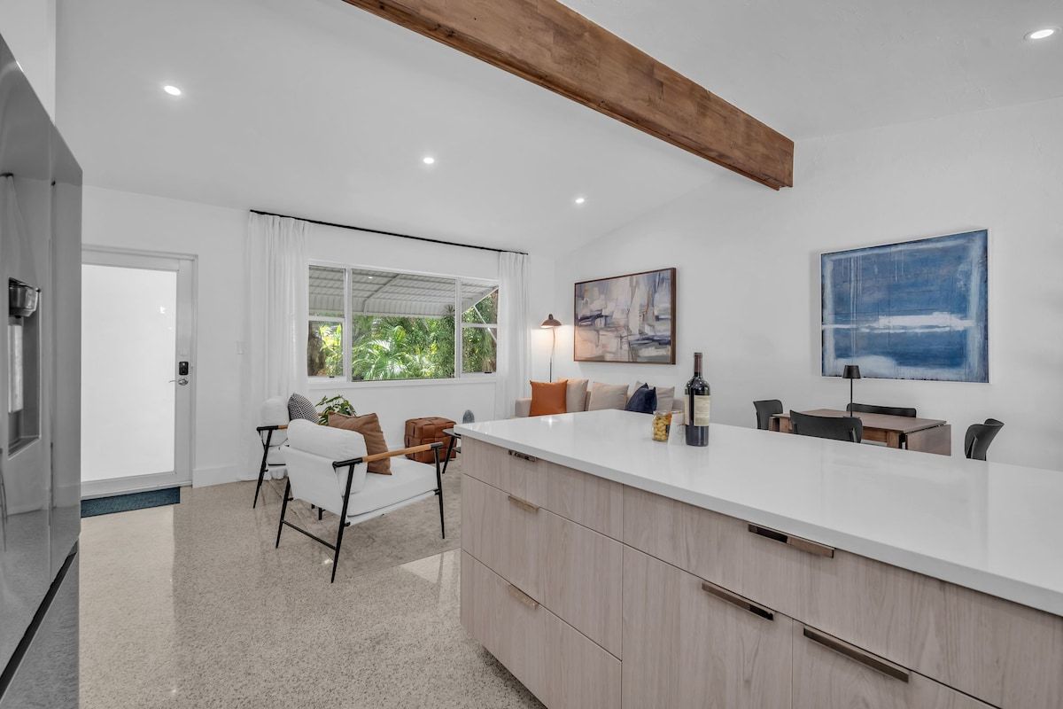 A modern kitchen with a large island, white cabinetry, and a dining area with chairs and a table.