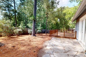 A stone patio leading to a wooden deck with a metal gate, surrounded by trees and a wooden fence. - Pinehurst Home Away From Home (Pinehurst)