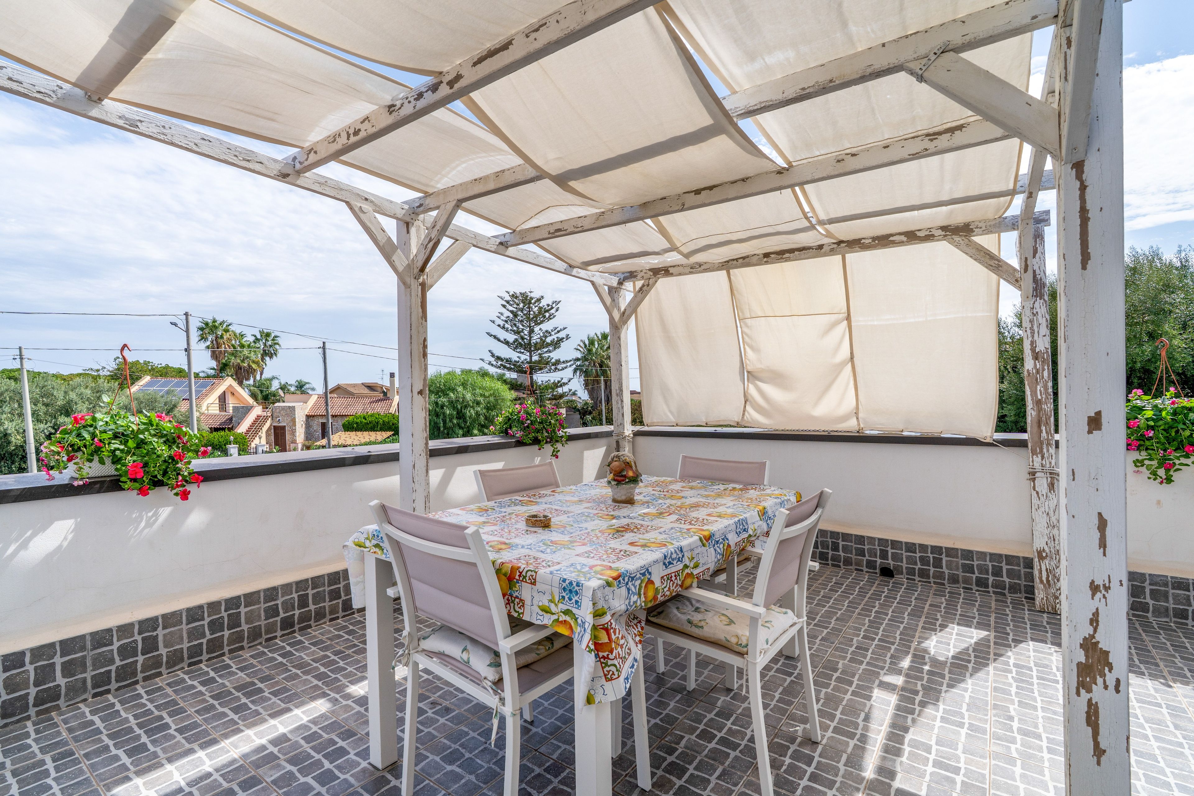 Eine überdachte Terrasse im Freien mit Tisch und Stühlen, einem gefliesten Boden und Blick auf die Umgebung.