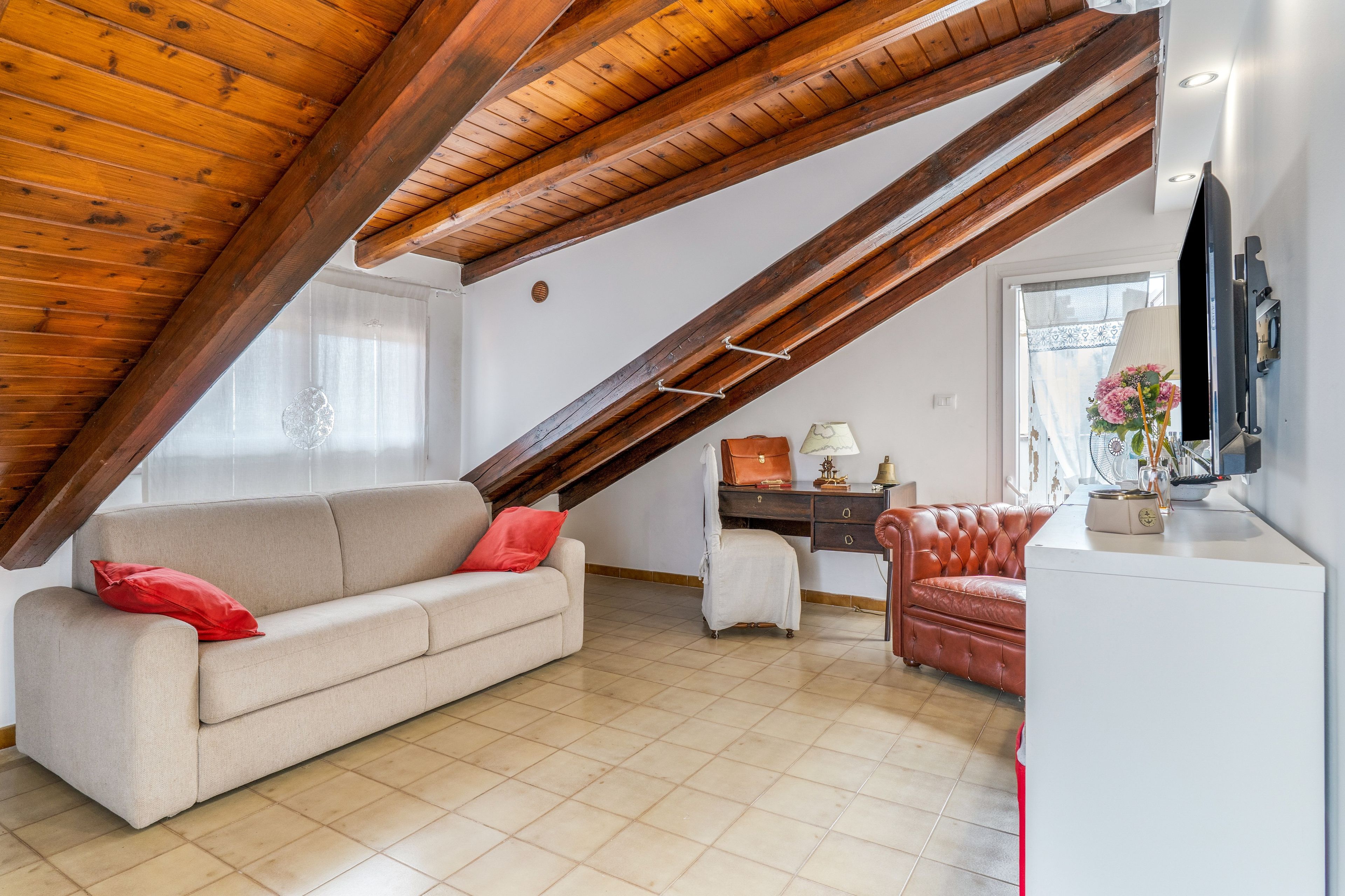 Ein Loft-Zimmer mit schrägem Dach, einer Couch, einem Sessel, einem Schreibtisch und einem Fernseher.