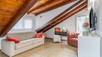 Une pièce de style loft avec un plafond en pente, un canapé, un fauteuil, un bureau et un téléviseur.