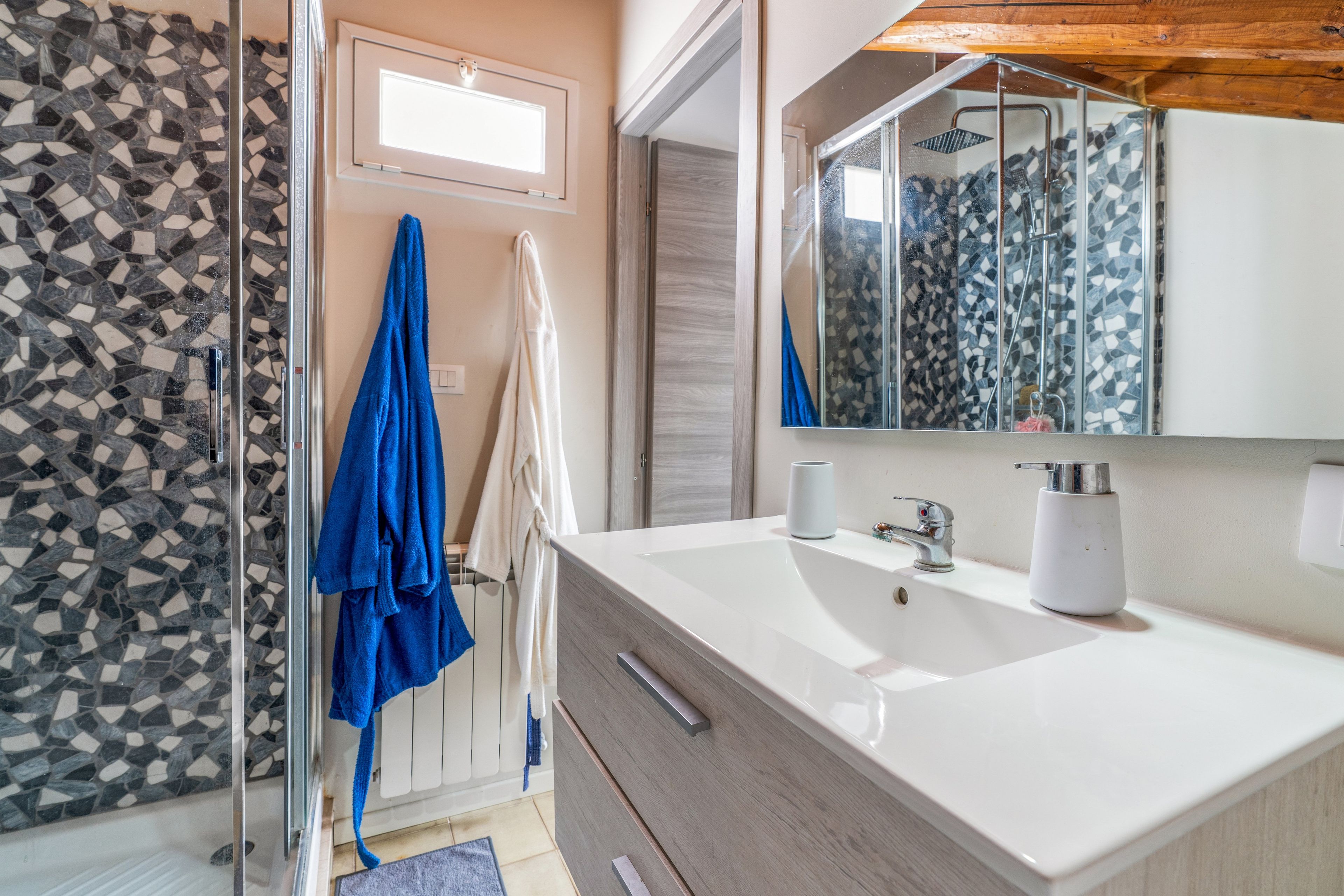 A bathroom with a white sink, a mirror, and a shower with mosaic tiles.