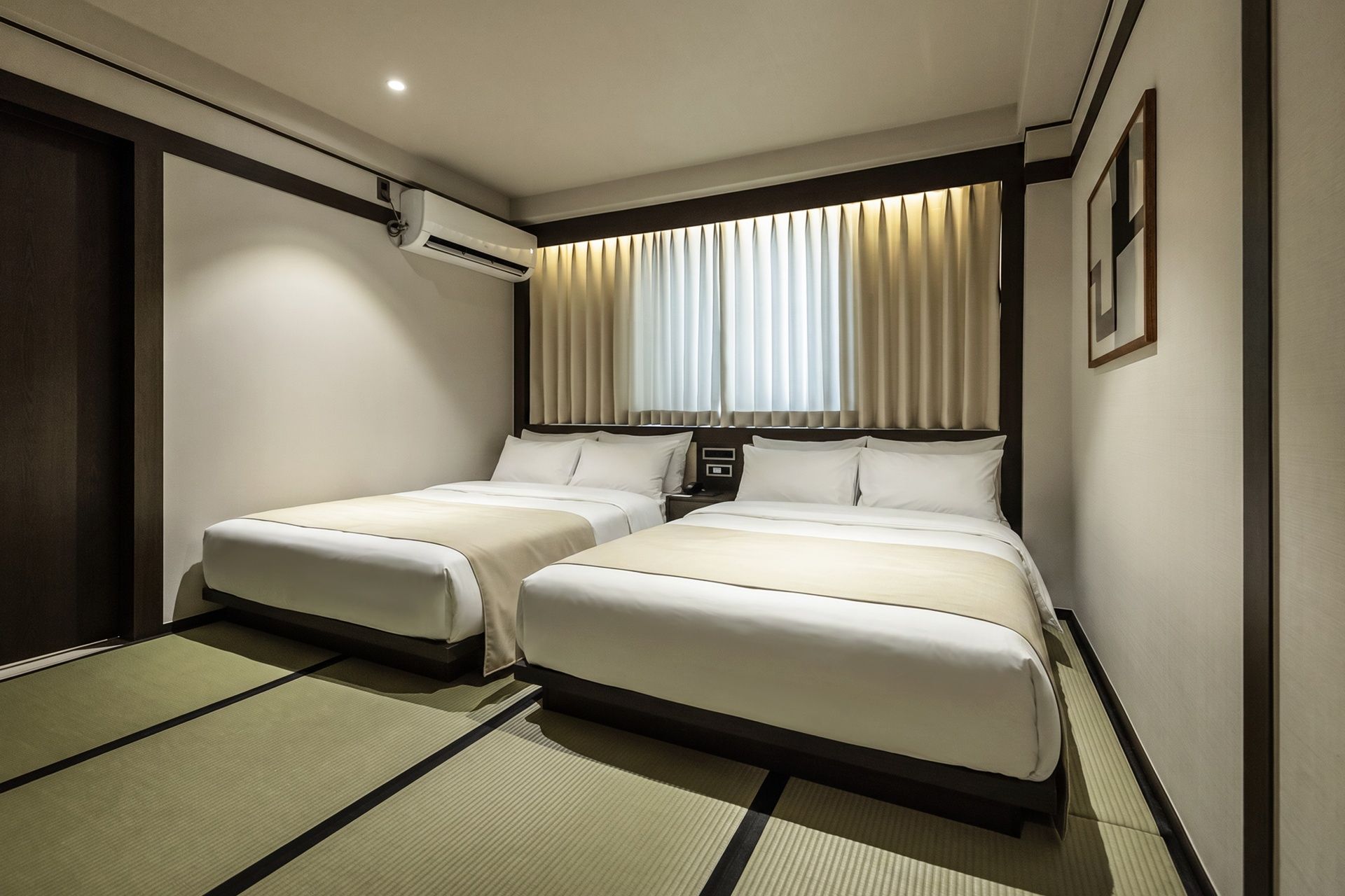 A hotel room with two beds, a wall-mounted air conditioner, and a window with curtains.