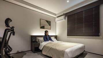Een slaapkamer met een bed, een nachtkastje, een wandairconditioner, een raam met jaloezieën en een loopband.