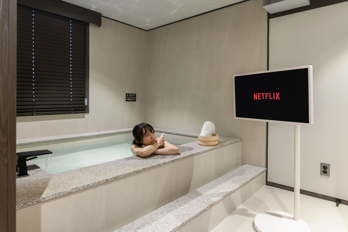 A modern bathroom with a bathtub, a toilet, and a television screen displaying 'NETFLIX'.