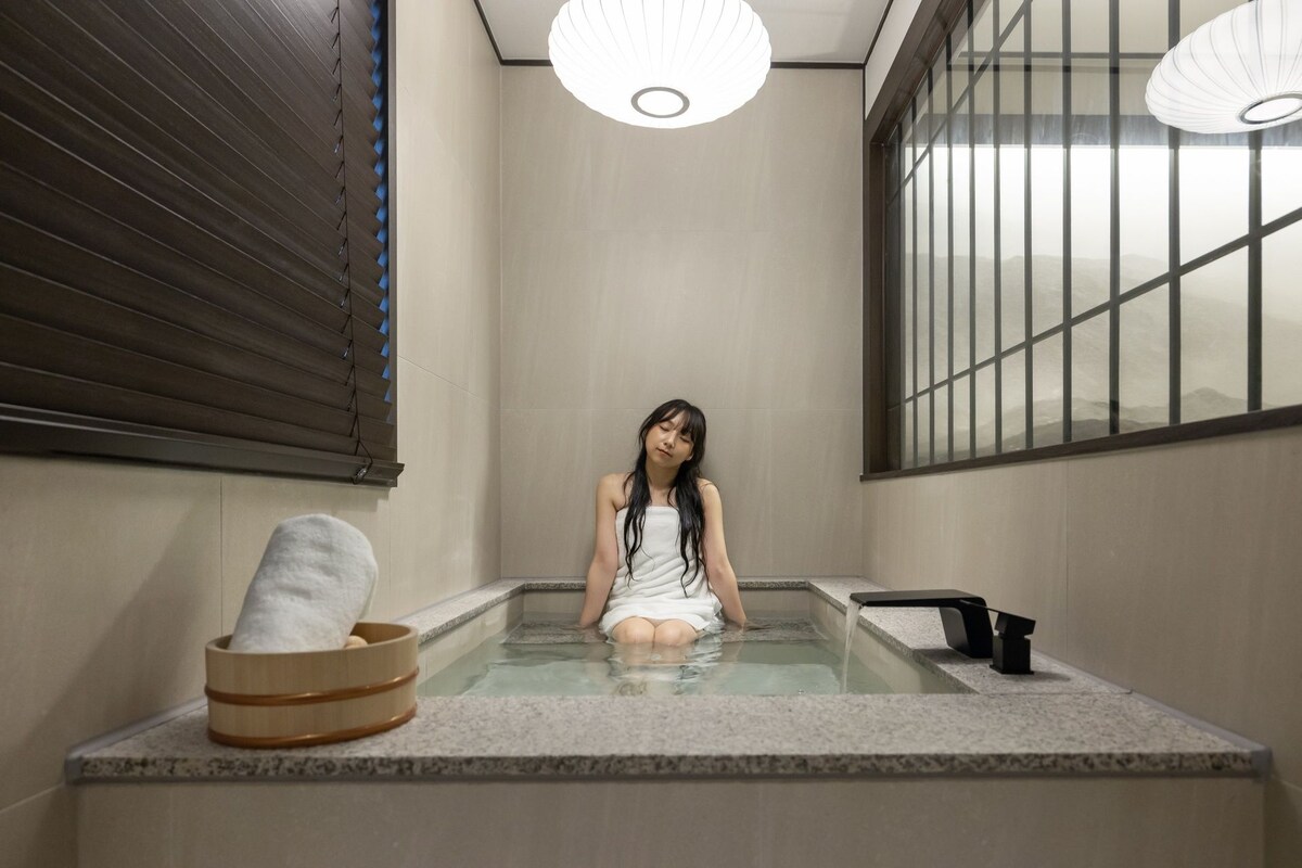 A person sitting in a hot spring bath with a wooden bucket and a black faucet.