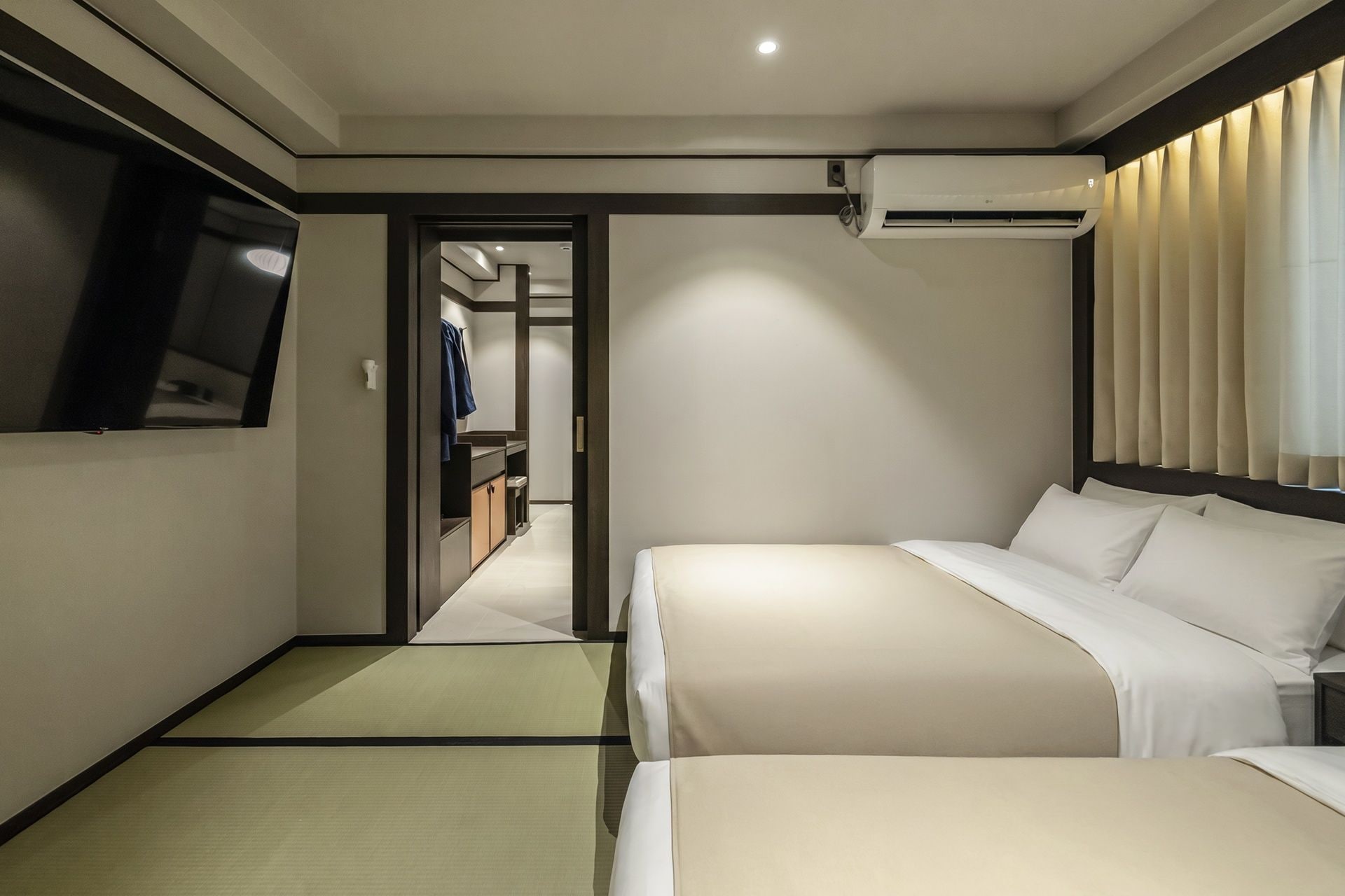 Habitación de hotel con cama, televisor, equipo de aire acondicionado y baño visible a través de una puerta abierta.