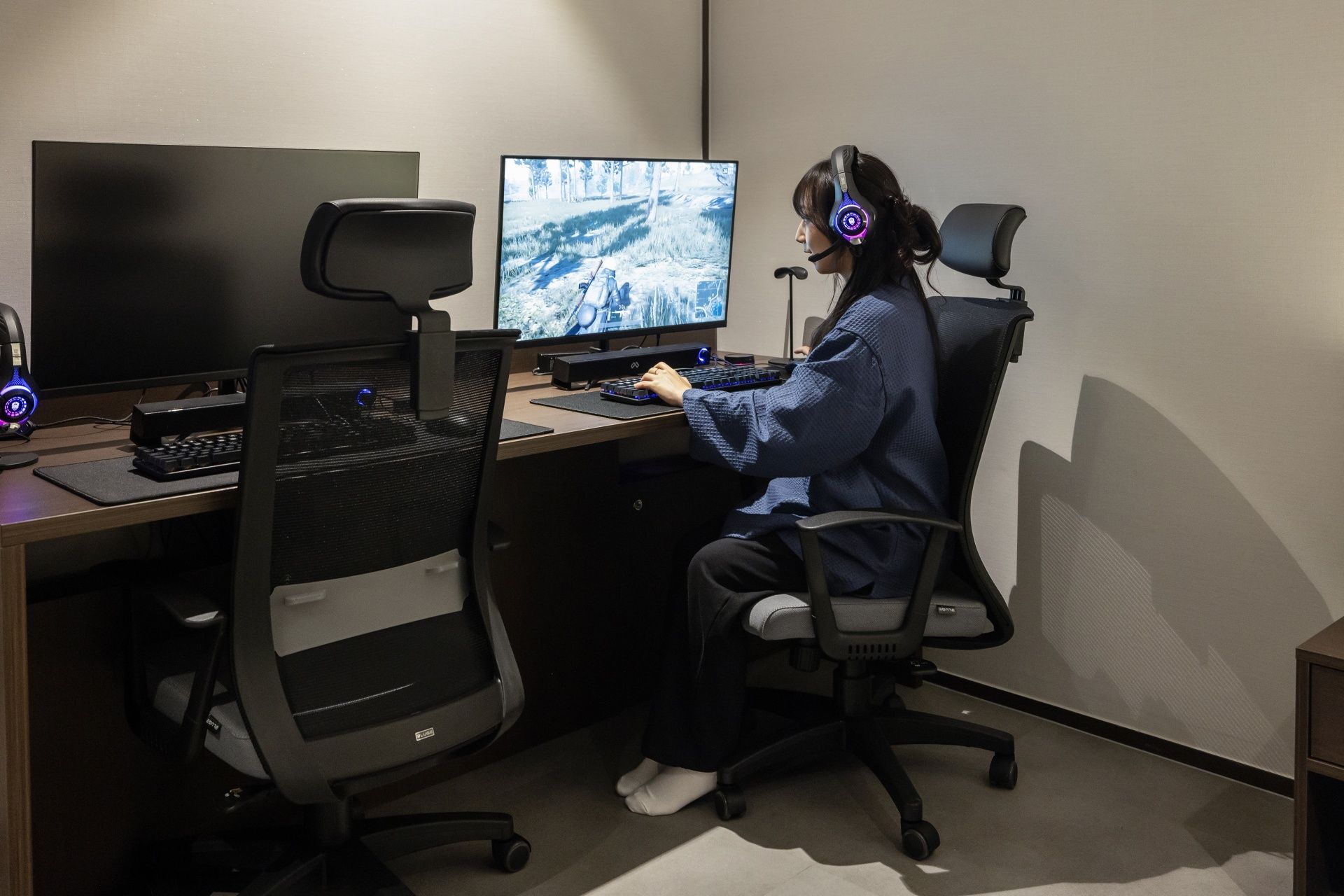 A person seated at a desk with a computer, keyboard, and headphones.