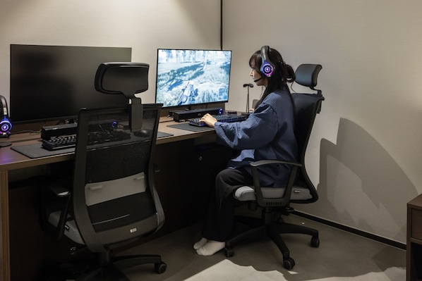 A person seated at a desk with a computer, keyboard, and headphones.