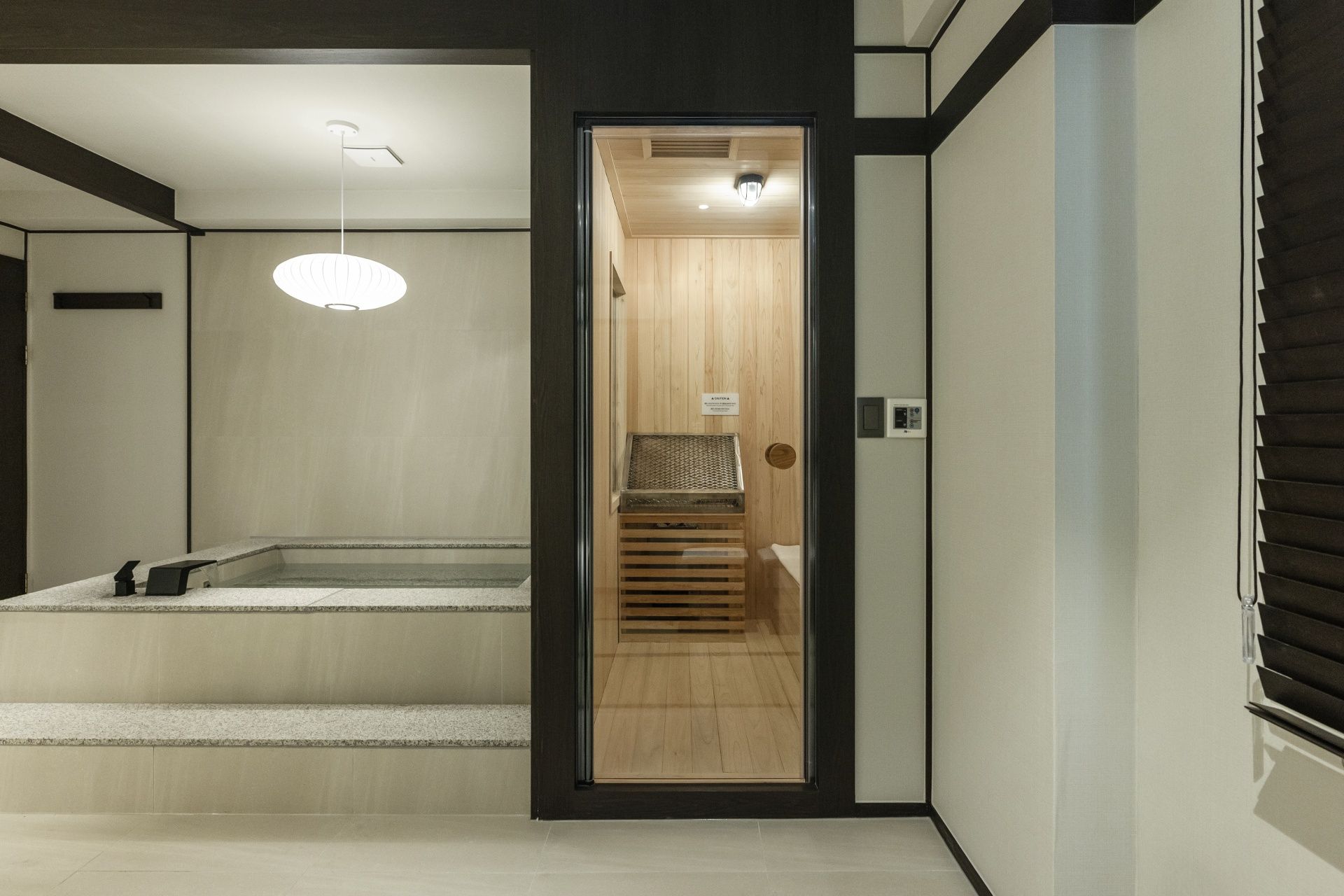 A modern interior with a wooden sauna, a bench, and a ceiling light fixture.