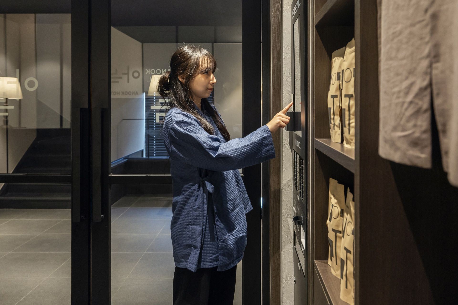 Persona interactuant amb un tancament digital a una porta de vidre, amb una escala i una paret que mostra la paraula 'AOKO' al fons.