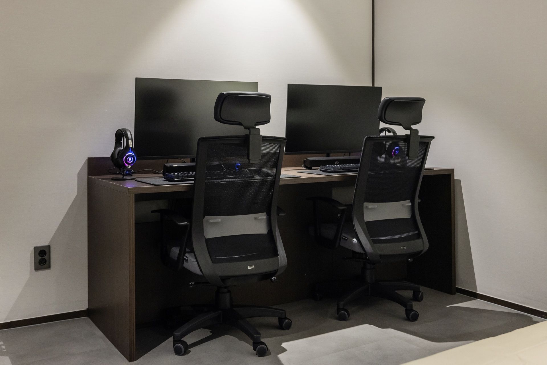Un espacio de oficina moderno con dos escritorios, cada uno con monitor de computadora, teclado y auriculares.