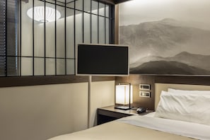 A hotel room with a bed, a nightstand, a wall-mounted TV, and a painting of mountains.