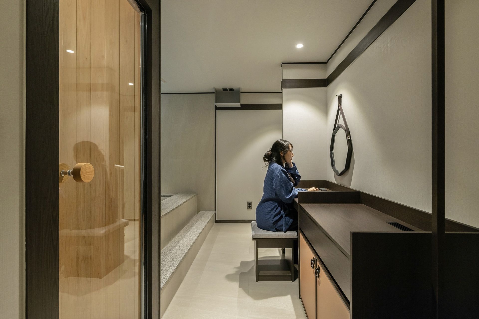 Ein modernes Interieur mit einer Holztür, einer Person, die an einem Tresen sitzt, und einer geometrischen Wanddekoration.