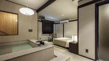 A modern hotel room with a bathtub, a bed, a desk, and a window with blinds.