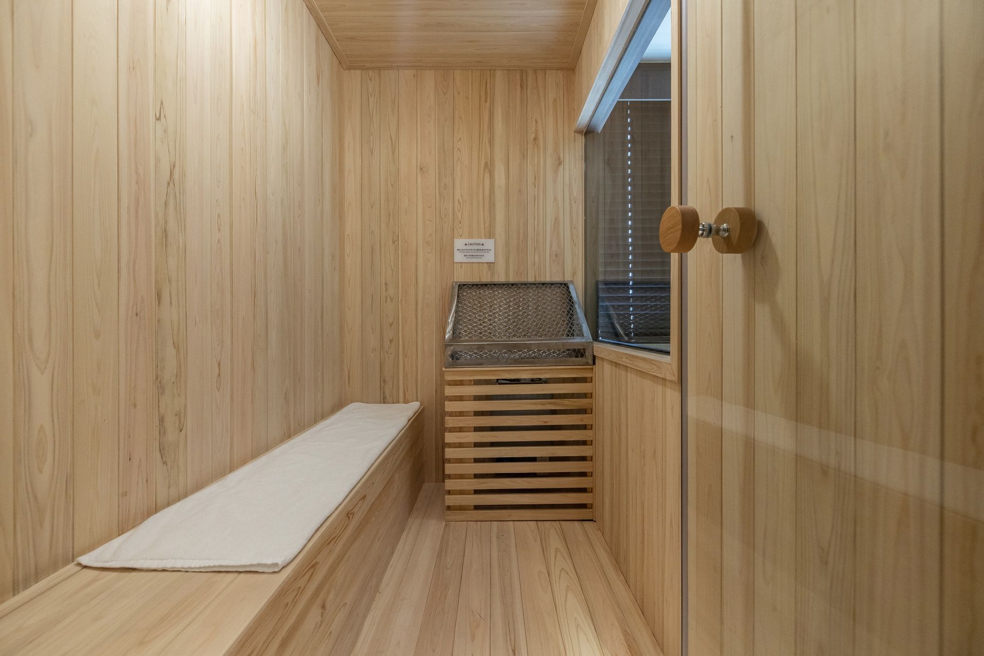A sauna room with wooden walls, a bench, a glass door, and a window.