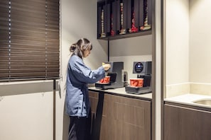 A person using a coffee machine in a room with a window, a shelf with items, and a sink.