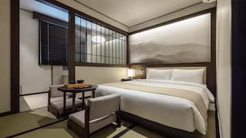 Una habitación de hotel con una cama, una mesita con una silla, una ventana con persianas y una lámpara de pared.