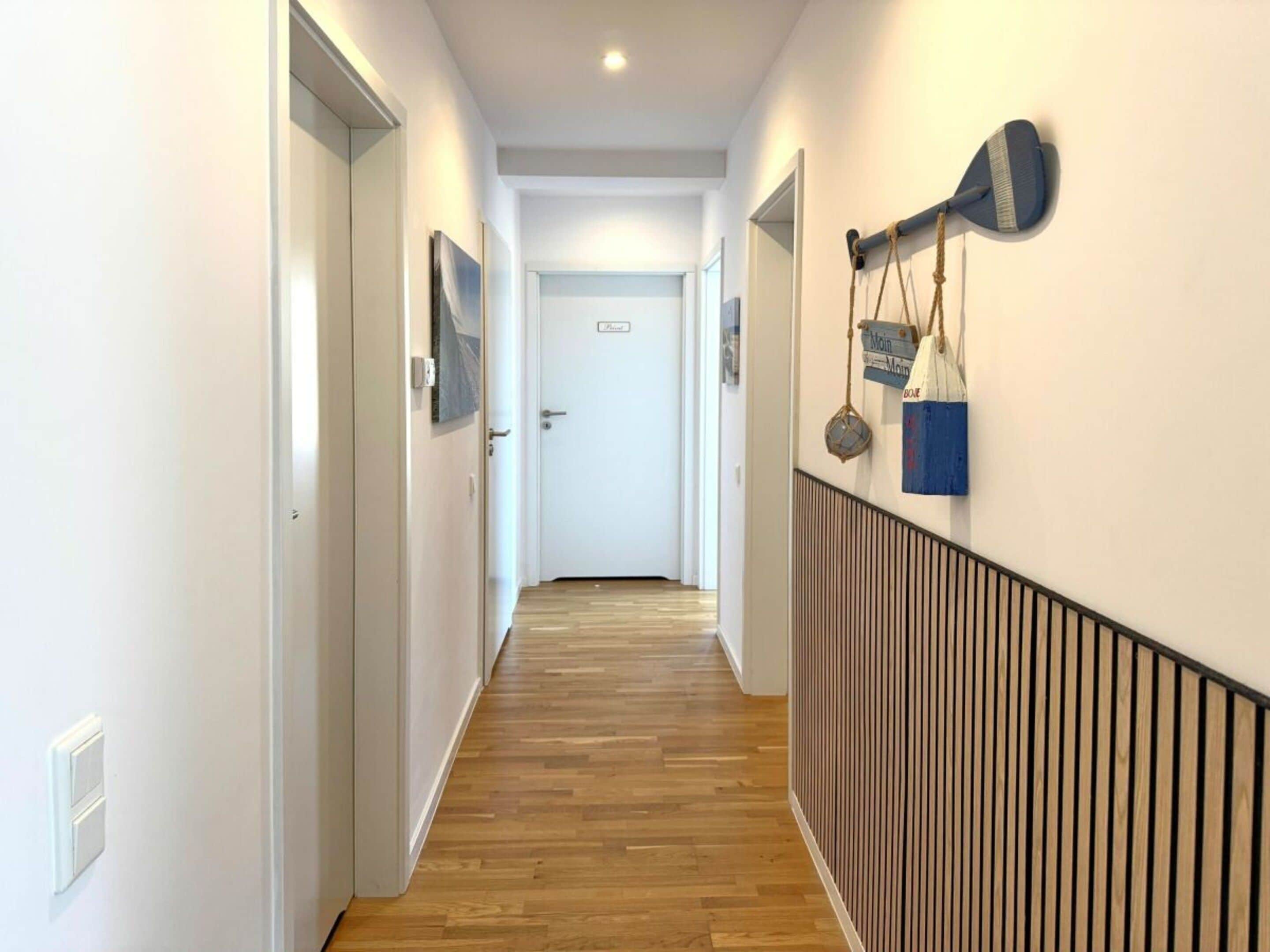 A hallway with wooden flooring, white walls, and a door at the end.