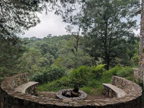 A stone bench with a fire pit in the center, surrounded by dense forest.