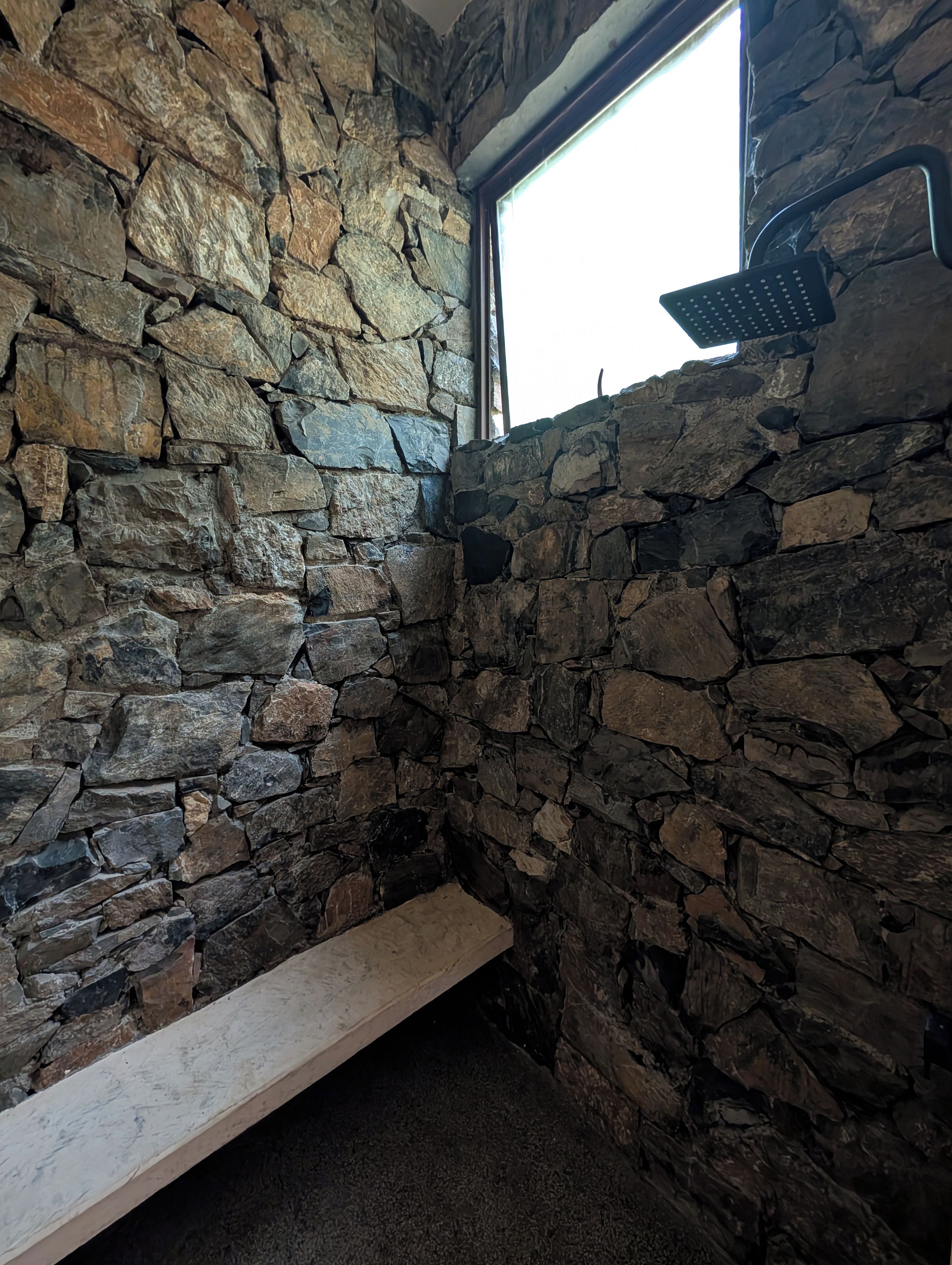 Habitación con paredes de piedra, una ventana y un banco.