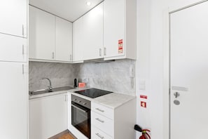A compact kitchen with white cabinets, a stainless steel sink, a black induction cooktop, and a built-in oven. - GuestReady - Cozy Retreat in Porto Center (Porto)