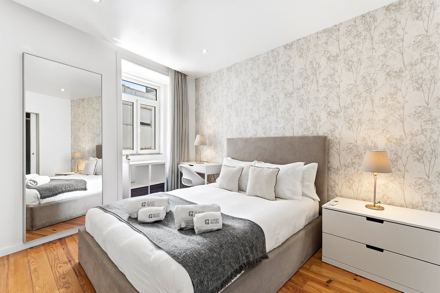 A modern hotel room with a large bed, bedside tables, a desk, and a mirror.