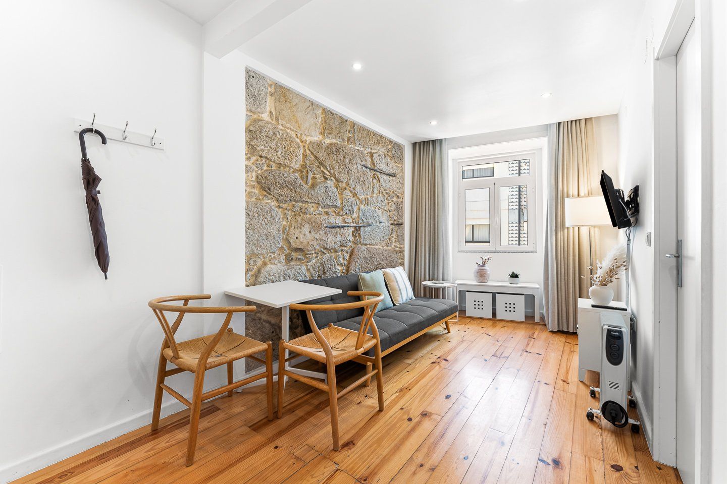 Een moderne woonruimte met een accentmuur van steen, een bank, een eettafel met stoelen en een compacte kitchenette.