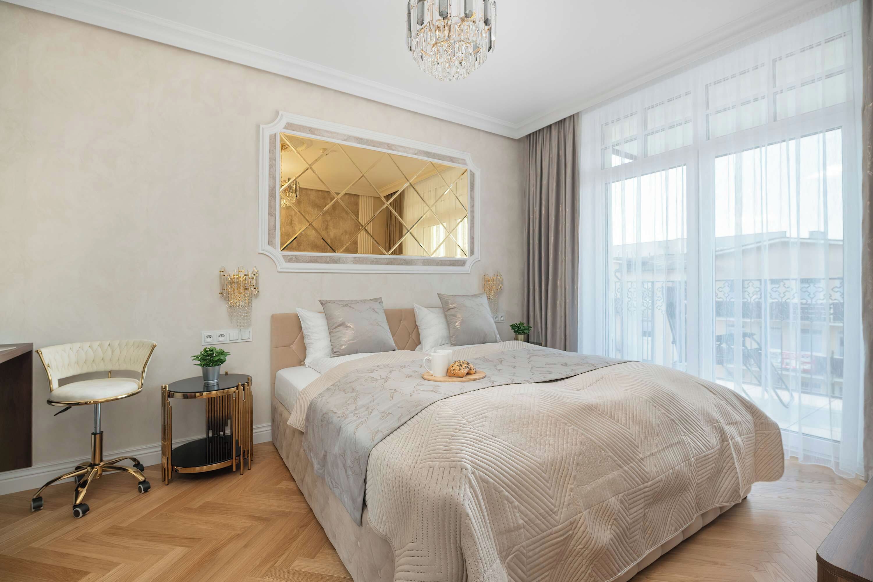Een hotelkamer met een groot bed, een bureau met stoel, een groot raam met gordijnen en een kroonluchter.
