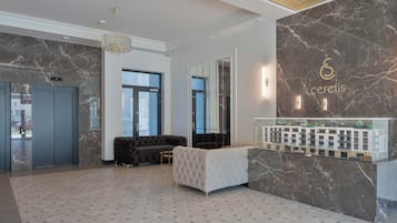 Ein moderner Empfangsbereich mit Marmorwand, einer Rezeption und einer Sitzecke inklusive Sofa und Sesseln.