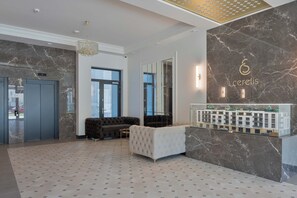 Un espace d’accueil moderne avec un mur en marbre, un comptoir d’accueil et un coin salon comprenant un canapé et des fauteuils.