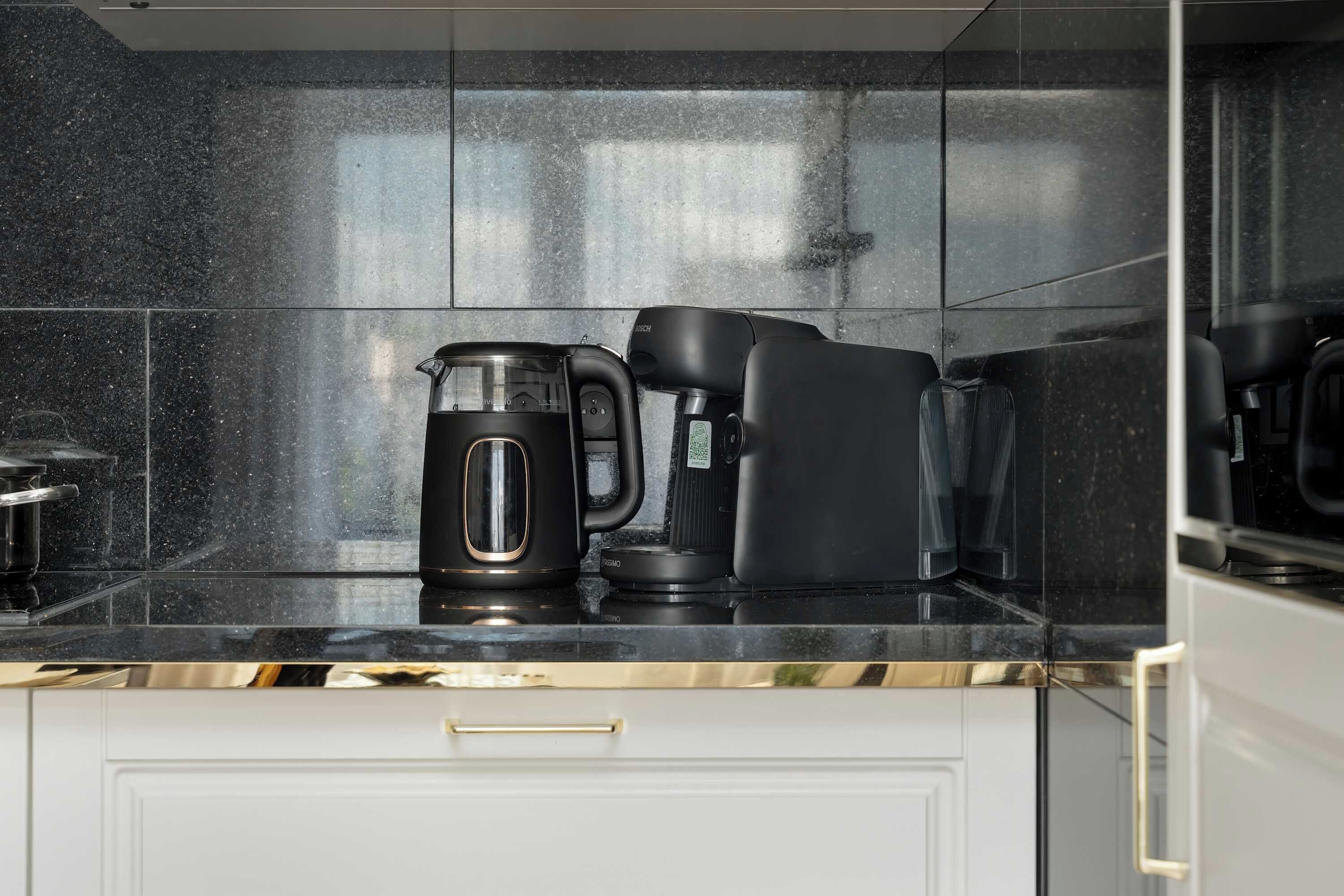 Une cuisine avec un plan de travail noir, une machine à café et une bouilloire.