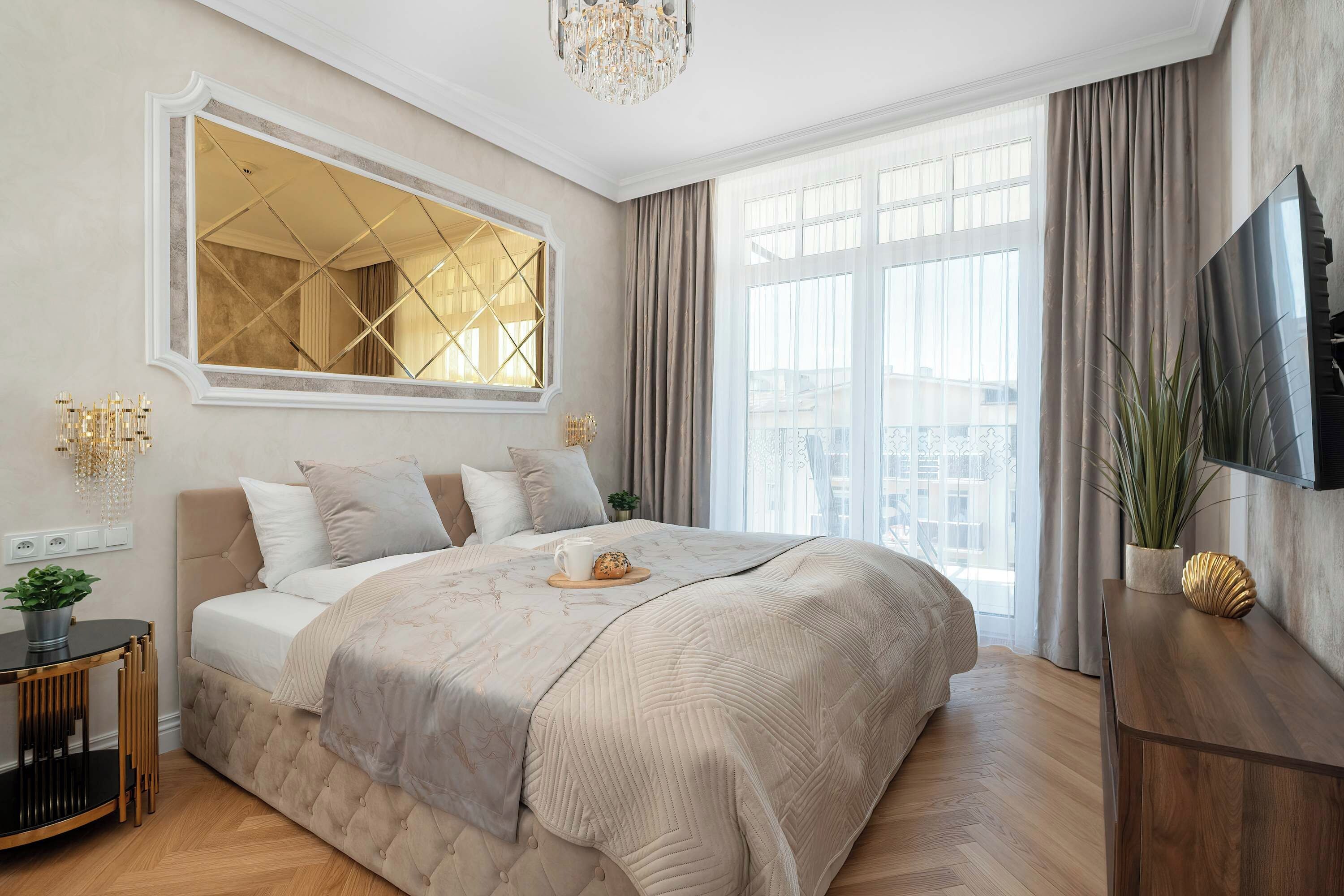 Ein Schlafzimmer mit einem großen Bett, einer Kristallleuchter, einem Fernseher und einem Fenster mit Vorhängen.