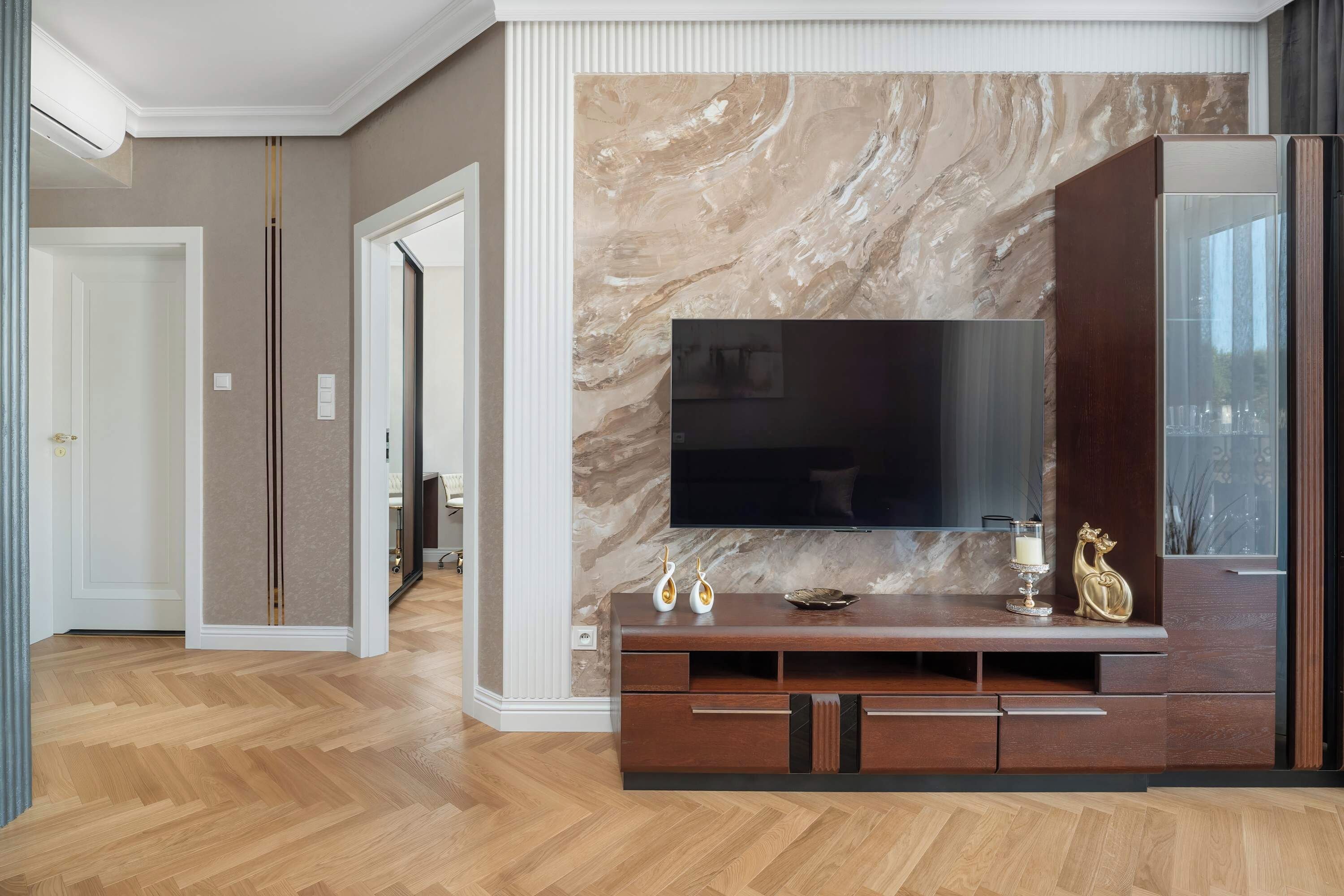 Een moderne woonkamer met een grote flatscreen televisie bevestigd aan een marmeren muur, houten vloeren en een donker houten entertainmentmeubel met decoratieve objecten.
