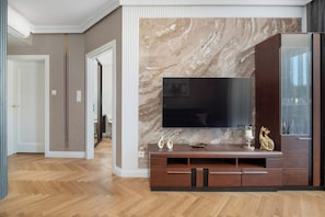 A modern living room with a large flat-screen TV mounted on a marble wall, wooden flooring, and a dark wood entertainment center with decorative items.