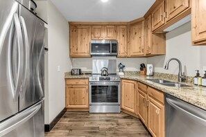 Eine moderne Küche mit Edelstahlgeräten, Holzschränken und Granit Arbeitsplatten, inklusive eingebautem Backofen.