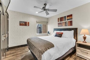 Une chambre à coucher avec un lit, un ventilateur de plafond, une fenêtre et des œuvres d’art accrochées au mur.